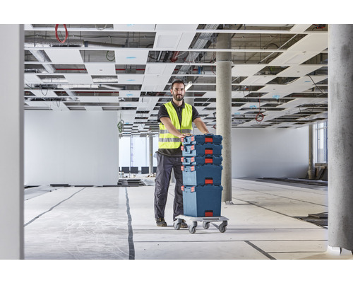 Handwerker transportiert Werkzeugkoffer auf einem Rollbrett in einem Rohbau.