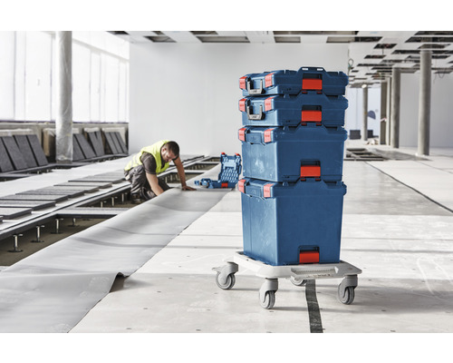Stapelbare Werkzeugkoffer auf Rollbrett in einer Baustelle mit Arbeiter