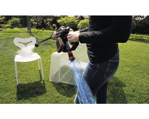 Eine Person benutzt einen Akku-Hochdruckreiniger im Garten, um einen Stuhl zu reinigen. Eine Wasserflasche ist an den Hochdruckreiniger angeschlossen.