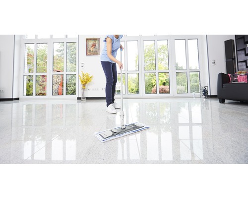 Frau wischt den Boden mit einem Mopp in einem hellen Raum mit großen Fenstern