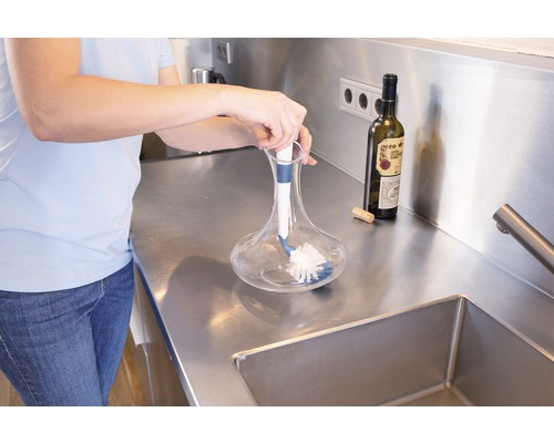 Eine Person reinigt eine Glaskaraffe mit einer Reinigungsbürste in der Küche.