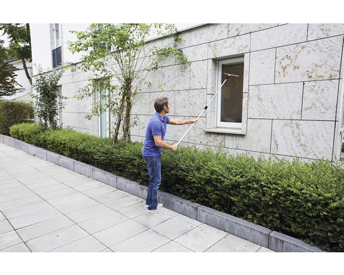 Ein Mann reinigt mit einem Fensterwischer an einer Stange ein Fenster.