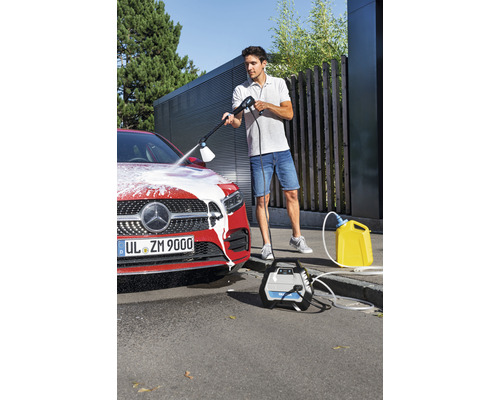 Ein Mann reinigt ein Auto mit einem Hochdruckreiniger, während eine gelbe Wasserkanister und das zugehörige Gerät daneben stehen.