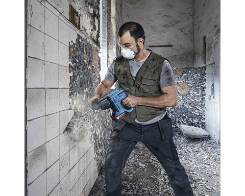 Handwerker mit Schutzmaske und Schutzbrille arbeitet mit einem Abbruchhammer an einer Wand.