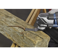 Eine oszillierende Multifunktionswerkzeug sägt einen Nagel aus einem Holzstück.