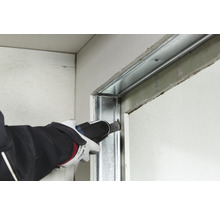 Ein Handwerker schneidet mit einem Multifunktionswerkzeug eine Metallstruktur an einer Gipskartonwand