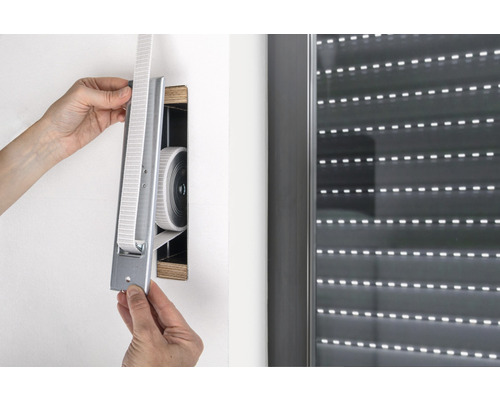 Person montiert einen Rollladengurtwickler an der Wand neben einem Rollladen.