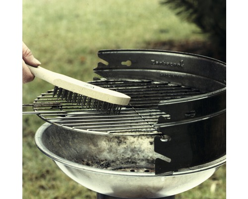 Eine Person reinigt einen Grillrost mit einer Grillbürste.