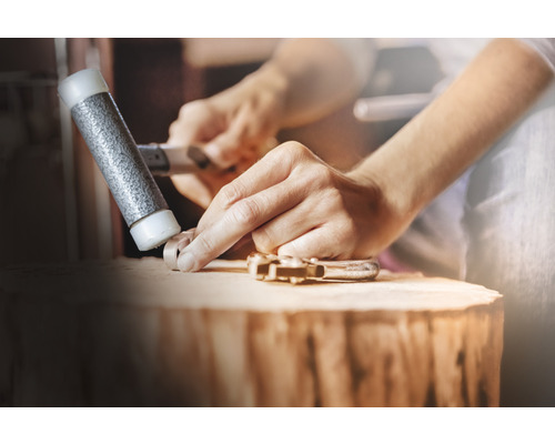 Mann formt ein Werkstück mit einem Hammer auf einem Holzblock.