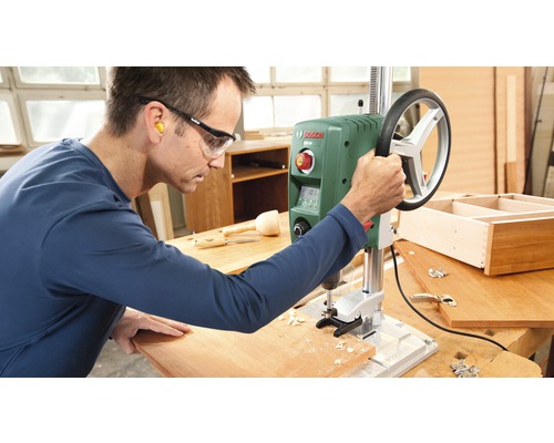 Ein Mann bedient eine Tischbohrmaschine in einer Werkstatt.