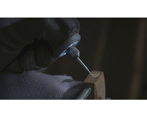 Detailaufnahme einer Hand mit Schutzhandschuh, die mit einem Gravierstichel in ein Metallobjekt eine Form graviert