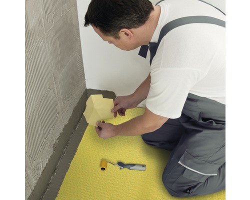 Handwerker verlegt Entkopplungsmatte auf dem Boden und an der Wand mit Werkzeug für Fliesenarbeiten