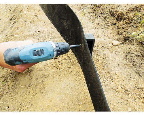 Eine Person befestigt mit einem Akkuschrauber eine Rasenkante aus Kunststoff.