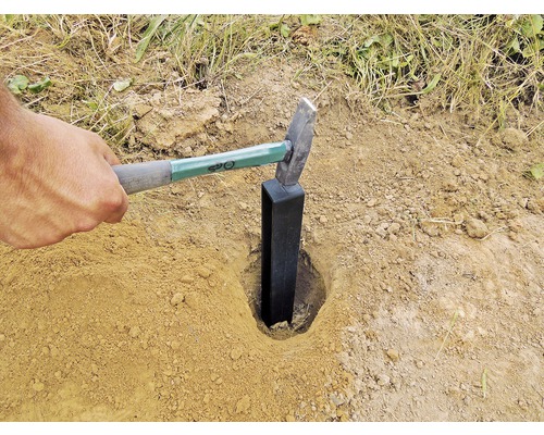 Ein Mann schlägt mit einem Hammer einen Zaunpfosten in den Boden.