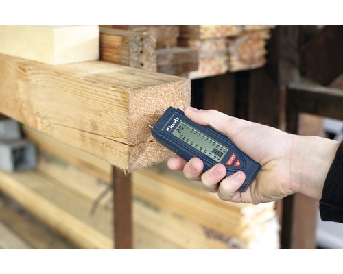 Eine Hand misst mit einem Feuchtigkeitsmesser die Feuchtigkeit eines Holzstücks.