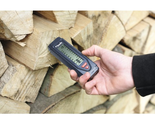 Hand misst Holzfeuchte mit einem Messgerät an Brennholzstapel