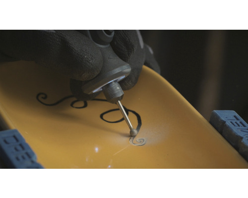 Eine Person graviert mit einem Multifunktionswerkzeug ein Muster in ein Werkstück.