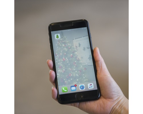 Ein Mobiltelefon wird gehalten und zeigt die Hornbach App mit einem Weihnachtsbaum im Hintergrund.