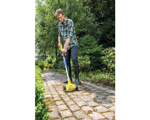 Ein Mann benutzt eine elektrische Fugenbürste zur Reinigung eines gepflasterten Weges im Garten.