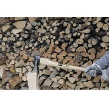 Holzhacken mit einer Axt vor einem Holzstapel.