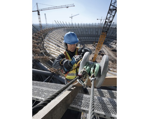 Ein Bauarbeiter mit Schutzhelm und Sicherheitsweste arbeitet mit einem Winkelschleifer auf einer Baustelle.