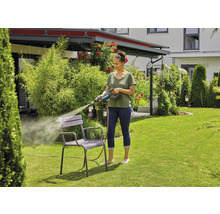 Frau reinigt Gartenstuhl mit Hochdruckreiniger im Garten.