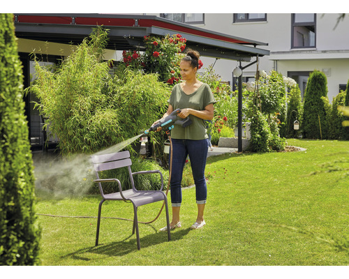 Frau reinigt Gartenstuhl mit Hochdruckreiniger im Garten.