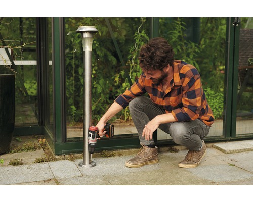 Ein Mann befestigt eine Solarleuchte mit einem Akkuschrauber im Garten.