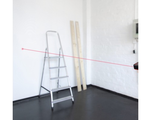 Raum mit Leiter, Holzbrettern und Laser-Entfernungsmesser mit rotem Laserstrahl