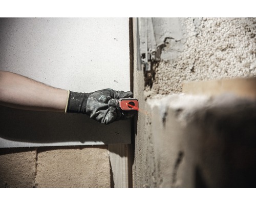 Eine Person verwendet ein Laser-Nivelliergerät an einer Wand, um ein Projekt auszurichten.