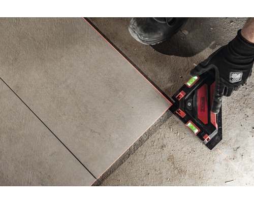 Ein Mann verlegt Fliesen mit einem Laser-Winkelmesser.