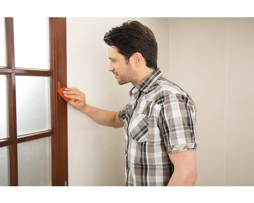 Mann entfernt Farbe von einem Holzfenster mit einem Farbschaber.