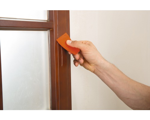 Eine Person verwendet einen Farbschaber zum Entfernen von Farbe von einem Fensterrahmen.