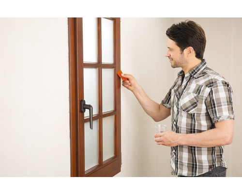 Mann reinigt Fenster mit Glasschaber