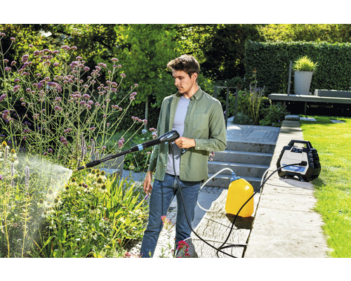 Mann benutzt einen Hochdruckreiniger im Garten zur Pflanzenbewässerung.