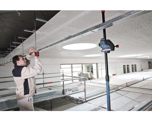 Ein Mann montiert eine Deckenkonstruktion mit einem Kreuzlinienlaser und einem Deckenstativ in einem Raum.