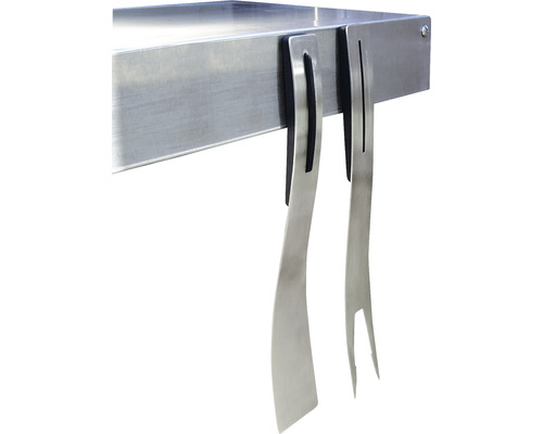 Grillzubehör wie Grillwender und Grillgabel aus Metall hängen an einem Grilltisch.