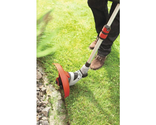 Person verwendet Rasentrimmer zur Rasenpflege im Garten.