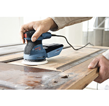 Ein Mann benutzt einen Bosch Exzenterschleifer, um eine Holztür abzuschleifen.