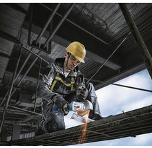 Ein Bauarbeiter mit Schutzhelm benutzt einen Winkelschleifer auf einem Gerüst.