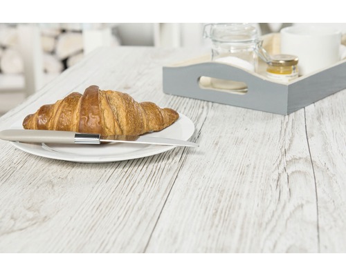 Ein Croissant mit einem Messer auf einem Teller und ein Frühstückstablett auf einem Holztisch.