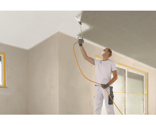 Eine Person sprüht Farbe mit einem Farbsprühgerät an die Decke eines Raumes.