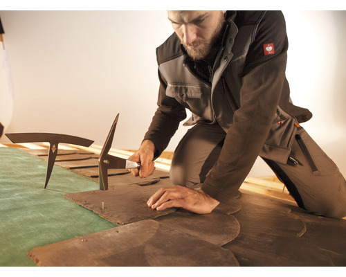 Ein Dachdecker bearbeitet Schiefer mit einem Schieferhammer.