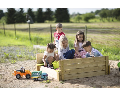 Fünf Kinder spielen in einem Sandkasten aus Holz im Garten.