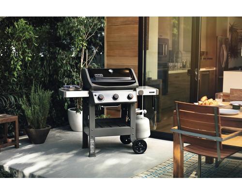 Weber Grill auf einer Terrasse mit Esstisch und Garten im Hintergrund