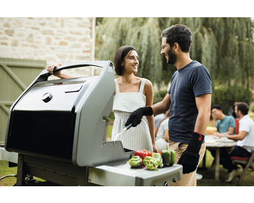 Ein Paar grillt mit einem Gasgrill im Garten. Auf der Grillfläche liegen Paprika.