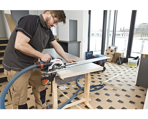 Handwerker sägt mit einer Handkreissäge ein Werkstück auf einer Werkbank. Ein Absaugschlauch ist an der Säge befestigt.