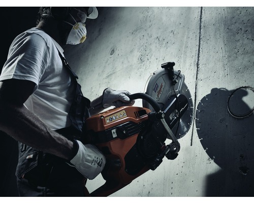 Ein Bauarbeiter schneidet mit einer Trennsäge einen Schlitz in eine Betonwand.