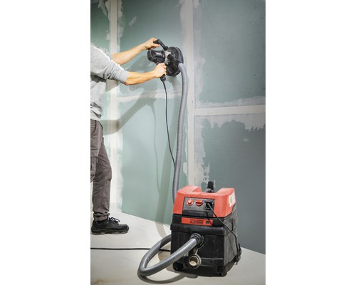 Mann schleift eine Wand mit einem Trockenbauschleifer, der an einen Staubsauger angeschlossen ist.