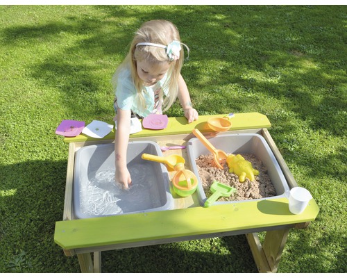 Mädchen spielt an Matschküche mit Sand und Wasser im Garten
